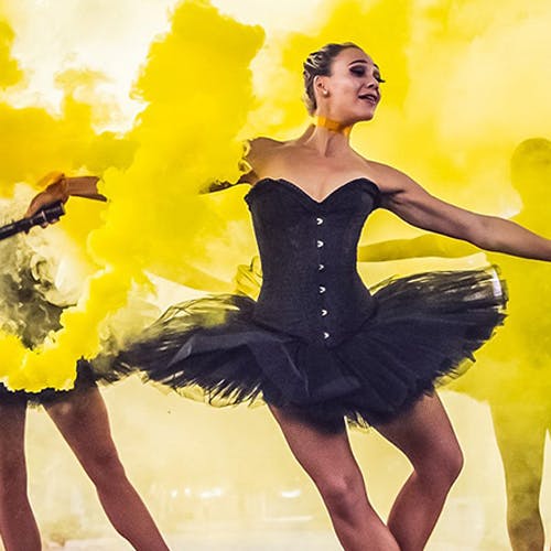 Ballerinas dancing around yellow smoke in black tutus