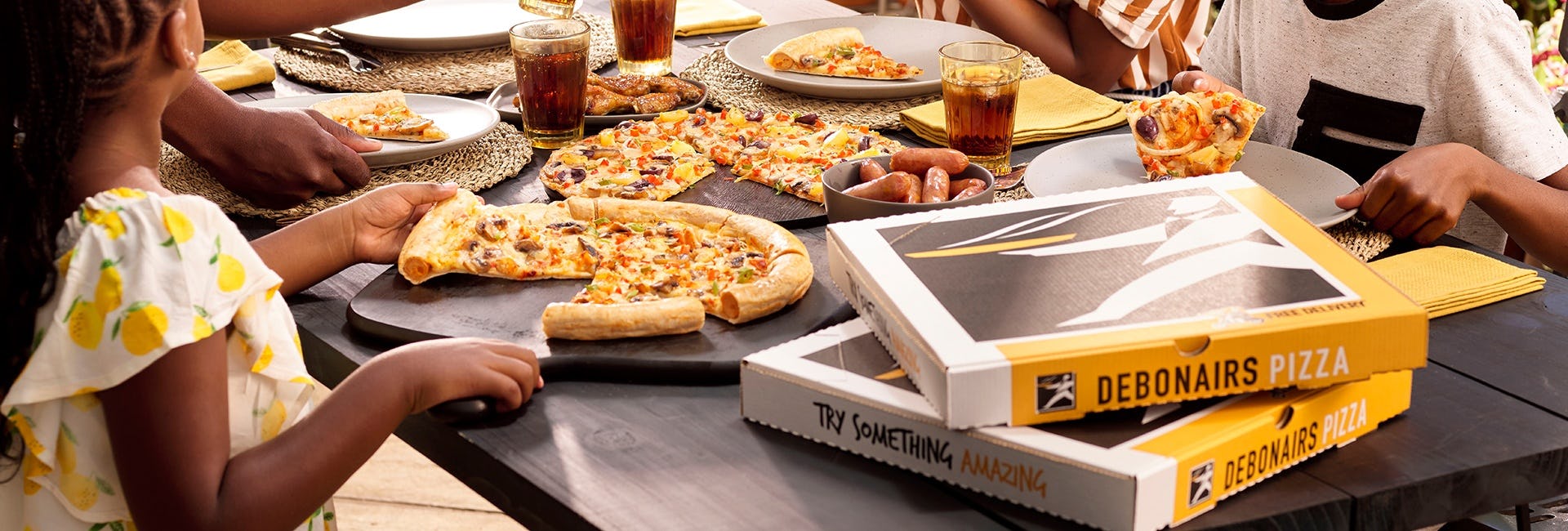 Pizza on a table with Debonairs pizza boxes