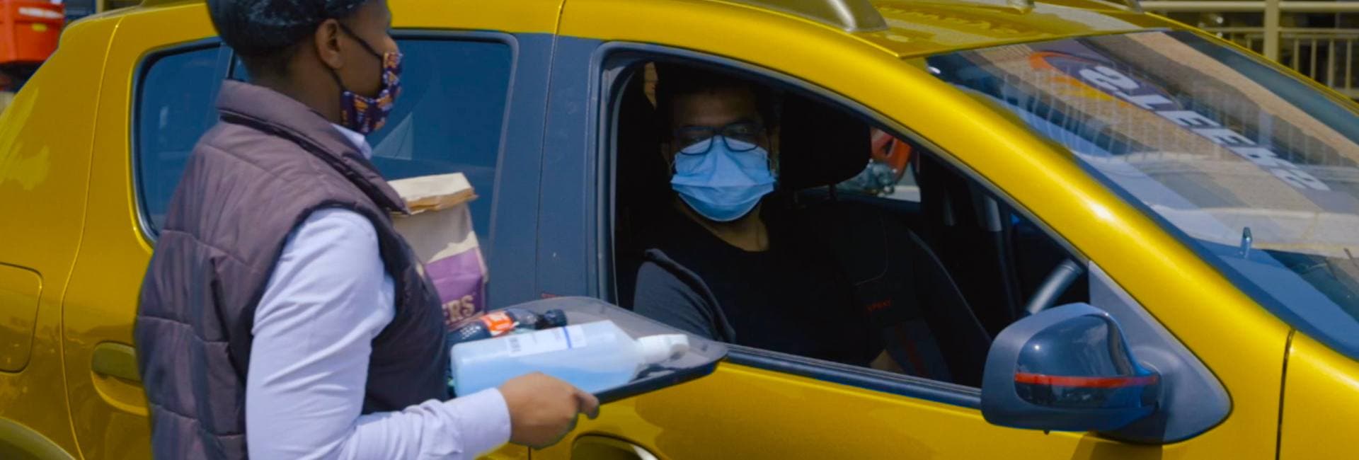 Person wearing a mask getting food delivered to their car
