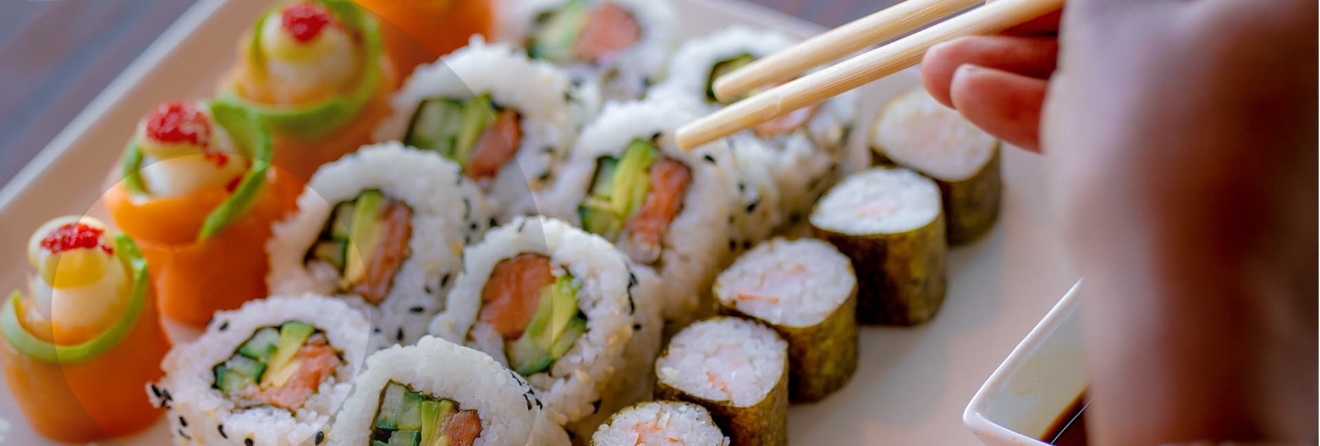 A selection of sushi on a plate with a hand holding chop sticks